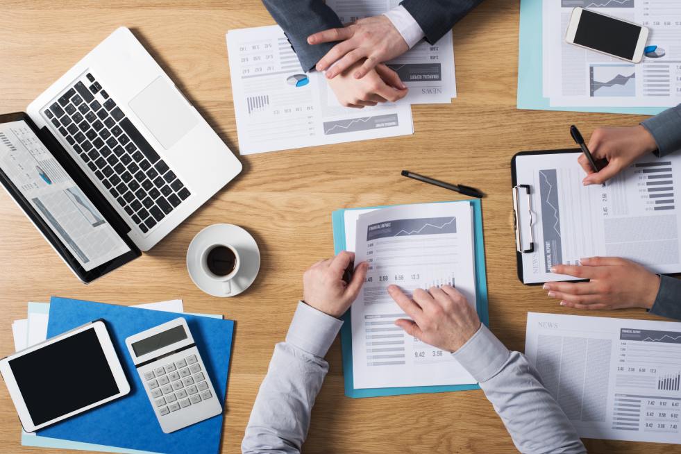 Group of professionals working around the table with laptop and charts and a cup of coffee